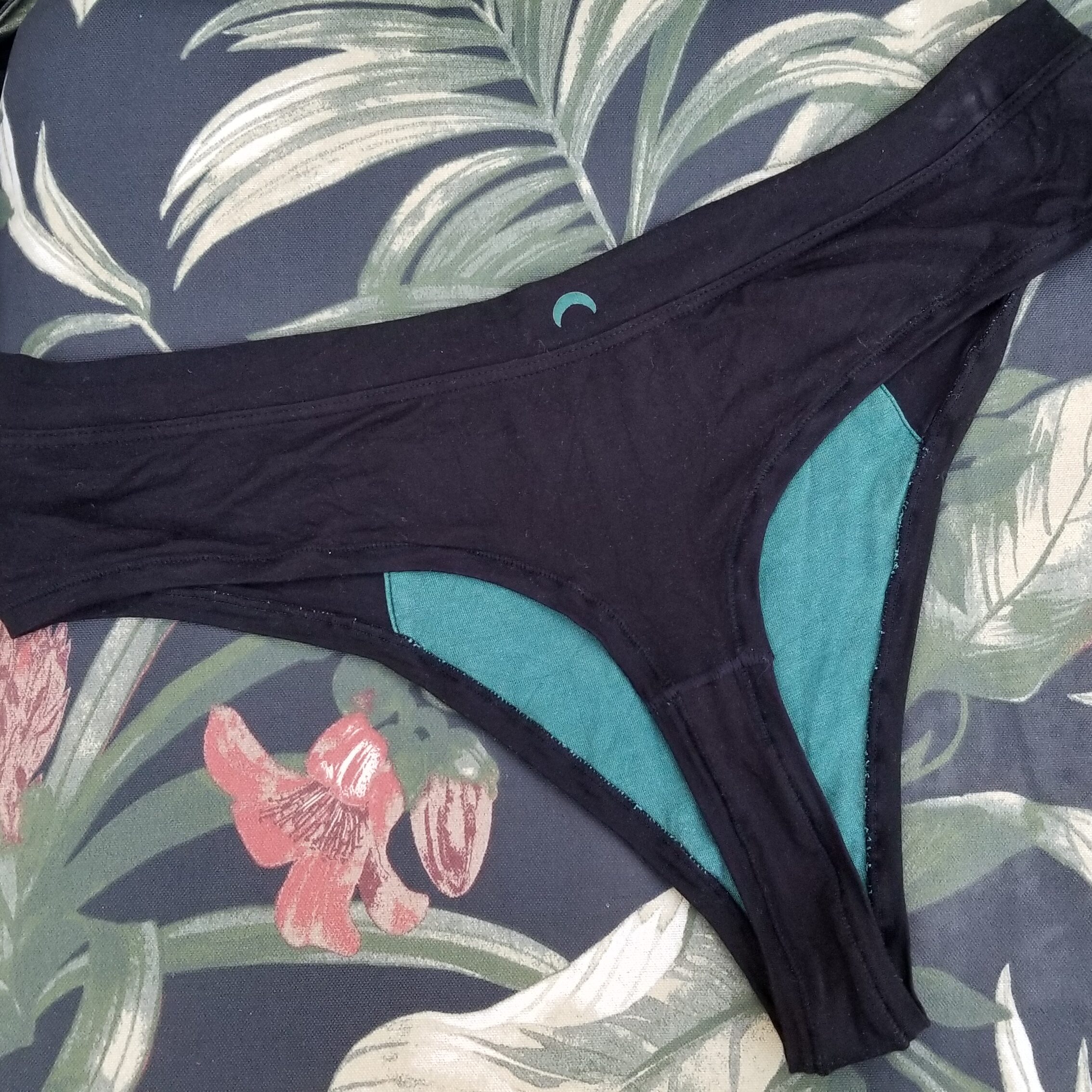 A black thong laid out flat on a tropical print background.