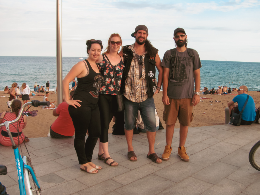 Four travelers pose in front of a beach in Barcelona. People are in the background and bikes are to the sides.